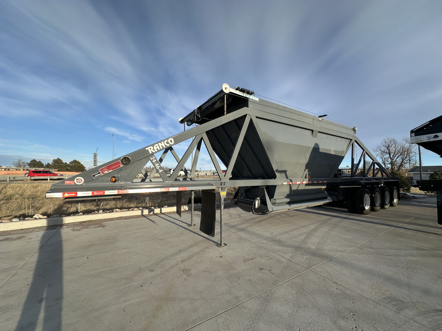 Ranco LW24464 dump trailer in an outdoor lot showing a long low-profile frame and hopper with support legs extended, gray metallic color.
