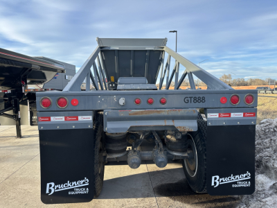Dump trailer rear showing GT888 marking, taillights, mud flaps with Bruckner’s Truck & Equipment logos, dual axles, and rear hitch assembly.