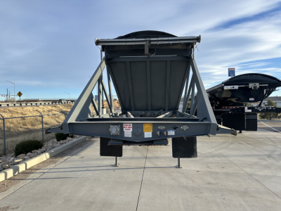 Dump trailer undercarriage showing LW24464 rear with hopper and frame, warning labels, and support legs visible.