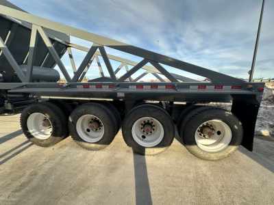 Trailer side view showing multiple axles and wheels on a dump trailer with structural truss frame and reflective tape.