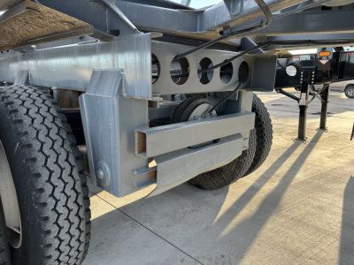Dump trailer undercarriage showing steel frame, dual wheels, and support braces with circular cutouts and hydraulic/air lines.