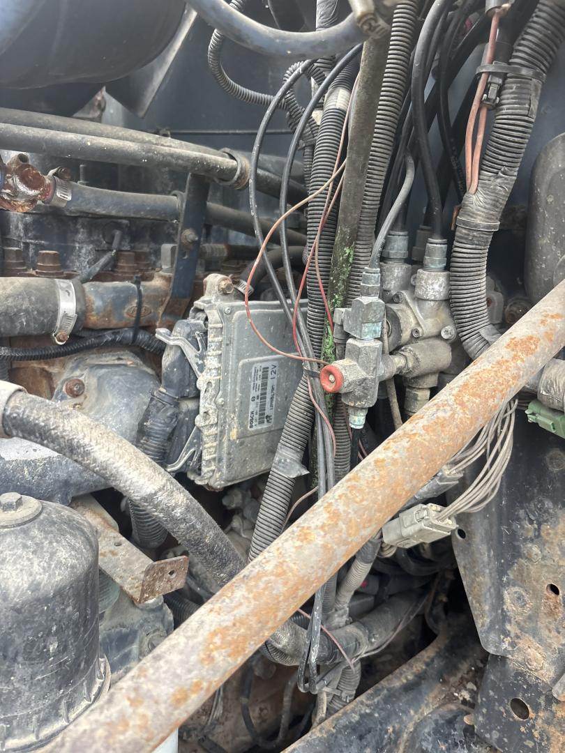 柴油发动机区域 showing electrical harnesses and control module mounted on engine bay with hoses and metal brackets.