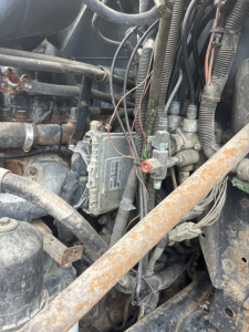 柴油发动机区域 showing electrical harnesses and control module mounted on engine bay with hoses and metal brackets.