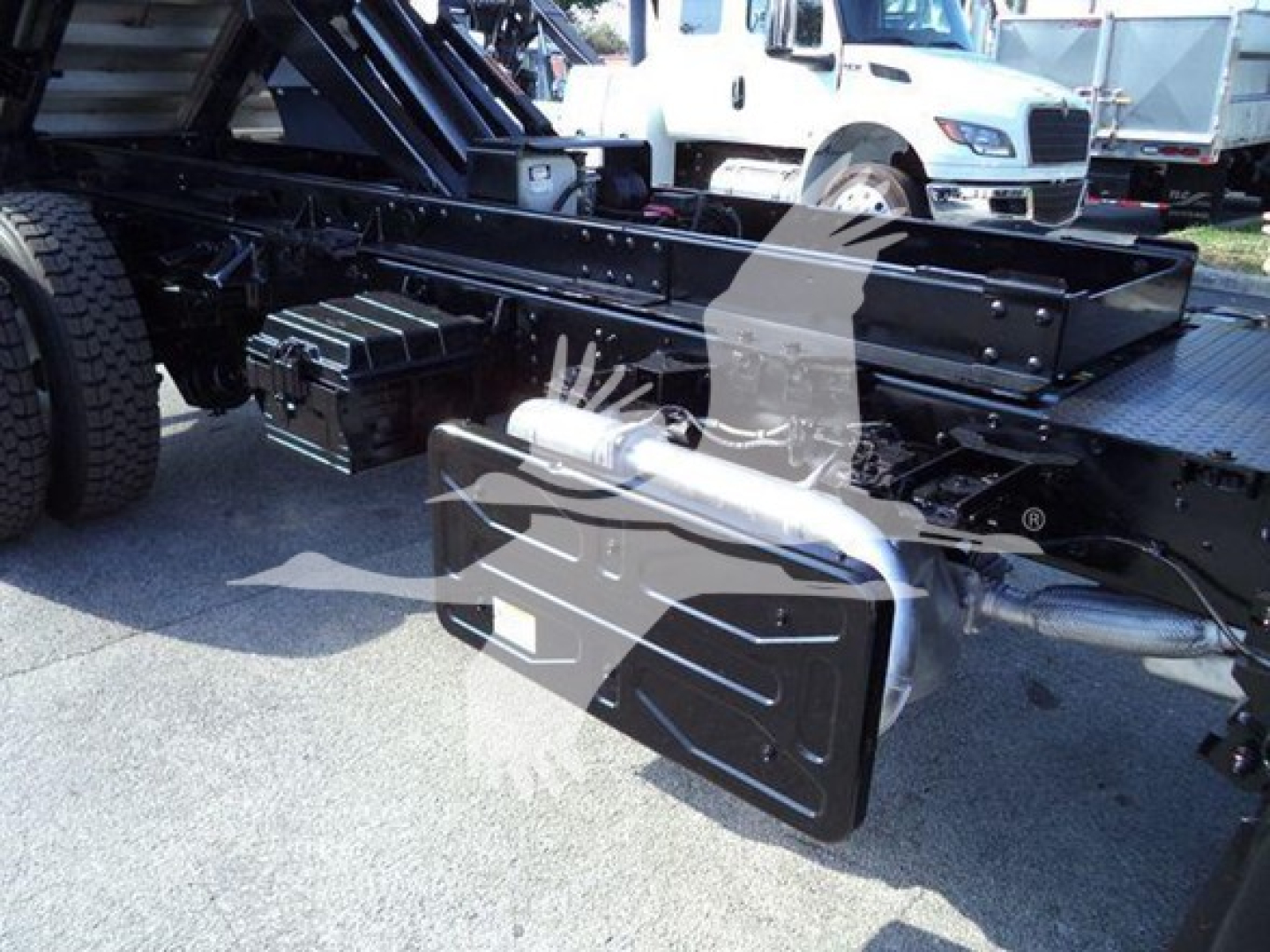Isuzu FTR chassis showing underbody tool box and frame rail with hydraulic equipment visible in background.