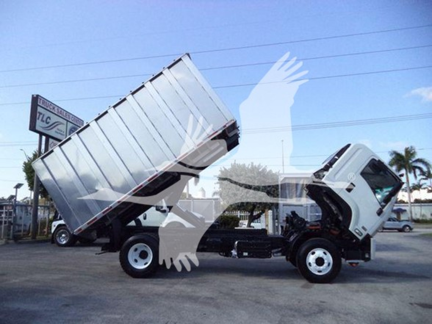 Isuzu FTR dump truck chassis with cab tilted forward, dual rear wheels, metal cargo bed raised in yard.