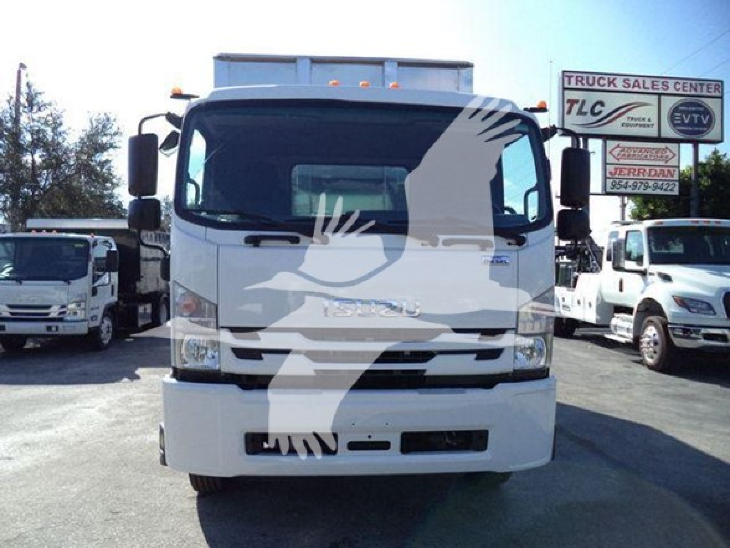 Isuzu cab of a 2018 FTR truck showing front grille, windshield, headlights, and side mirrors; signage in background includes TLC Truck Sales Center