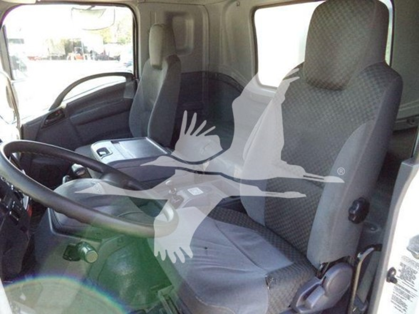 Truck cab interior with steering wheel and passenger seat visible; faint overlay of a logo on the image. Door and window frames show the Isuzu FTR cabin area.