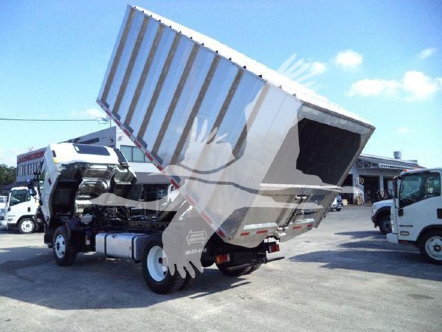 Isuzu FTR truck with dumping dump bed raised in a lot, side view shows cab and chassis, tilt bed in elevated position.