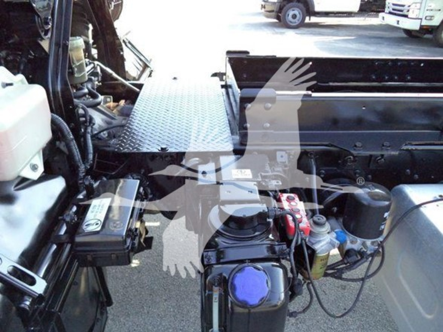 Isuzu FTR engine bay and dashboard area with exposed components, blue coolant cap, battery, hoses, and metal deck in foreground.