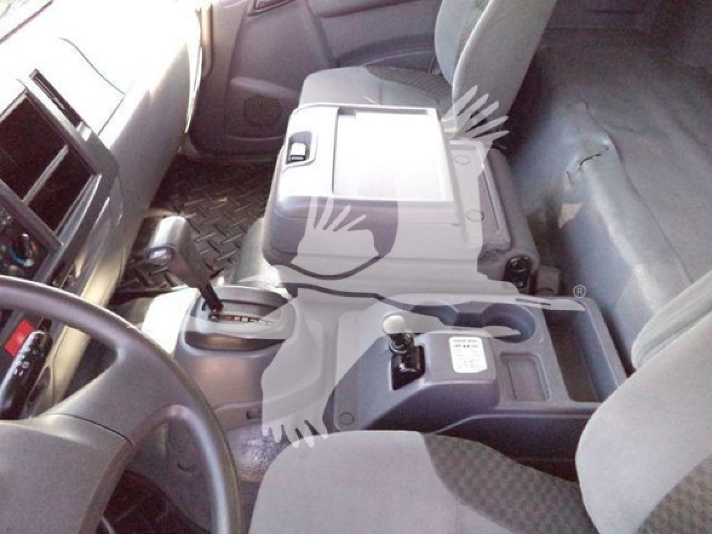 Isuzu FTR interior view showing center console with gear selector and cup holders; dashboard and passenger seat; metal floor plate visible. Text on console reads tiny labels not legible.