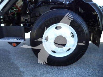 Isuzu truck front wheel with white rim and tire; partial engine bay visible; watermark overlay showing a bird graphic