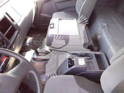 Isuzu FTR interior view showing center console with gear selector and cup holders; dashboard and passenger seat; metal floor plate visible. Text on console reads tiny labels not legible.