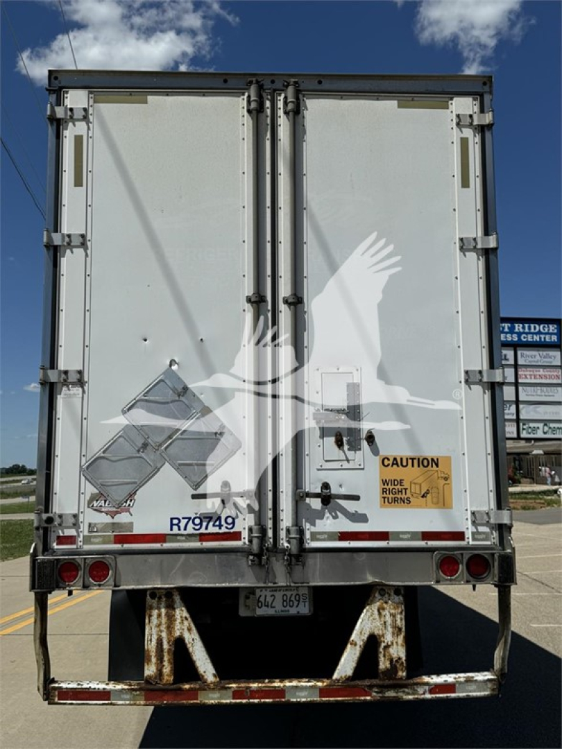 Reefer trailer rear view showing two doors with hinges, warning label, and reflective markings; license plate area and bumper with rust-like texture.