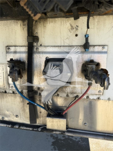 Trailer electrical connection panel on a Wabash reefer trailer showing two circular connectors, blue and red power lines, black wire harness, and a central rectangular filter or plug.