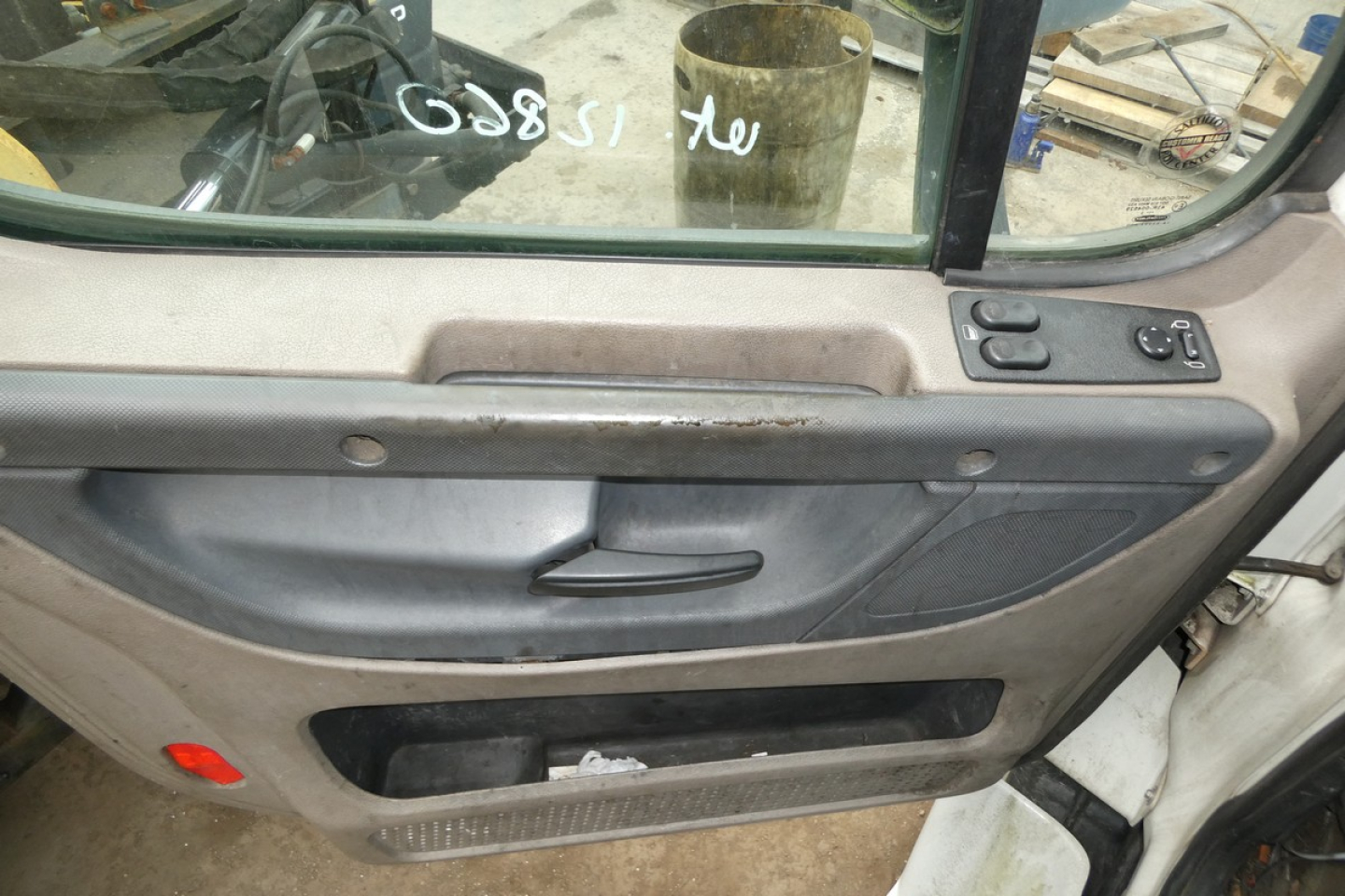 Truck door interior showing window controls and armrest with scratches; part of a beige cab door and side panel.
