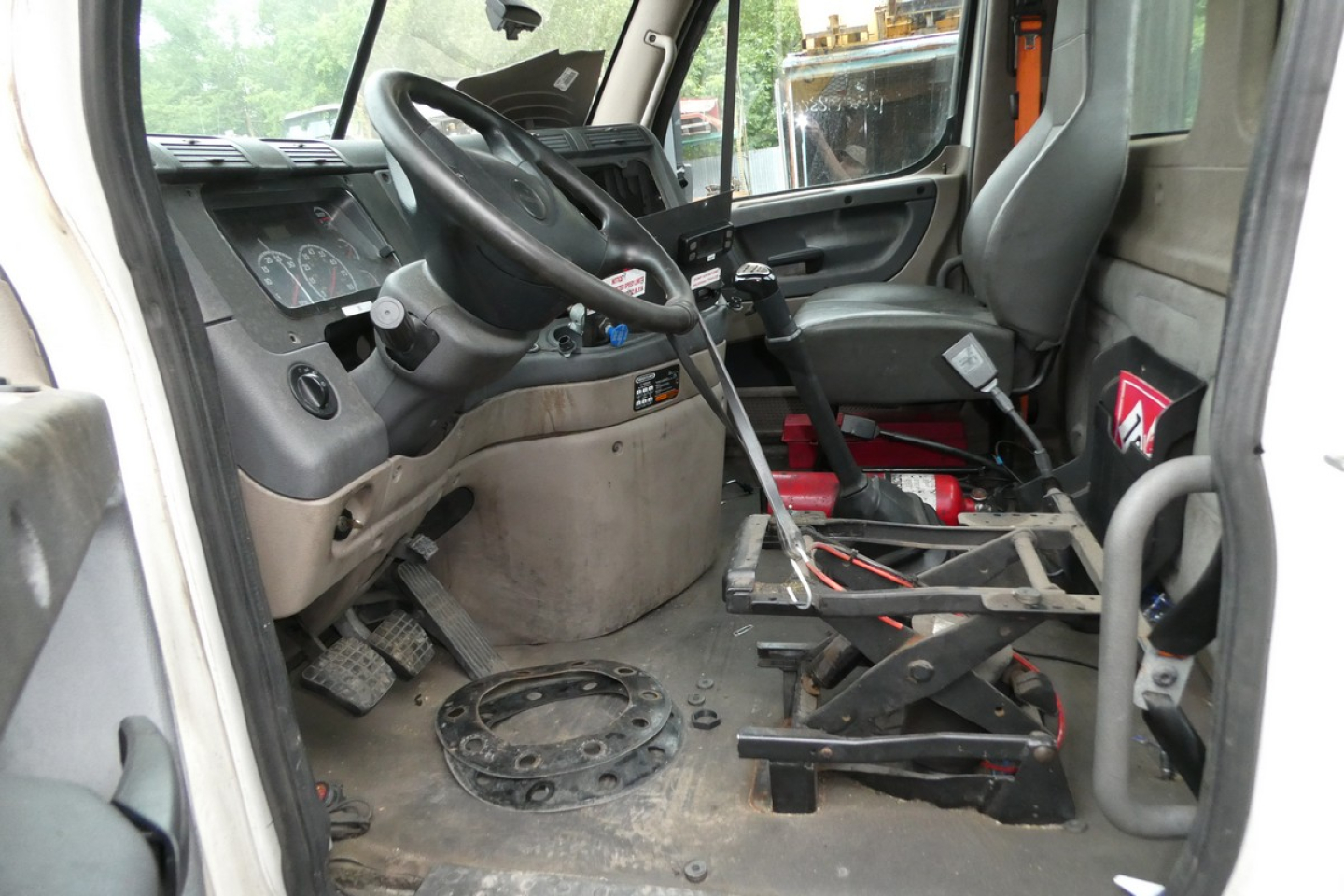 Cab interior of a 2014 Freightliner Cascadia 113 truck showing steering wheel, dashboard, and bare floor with exposed frame components.