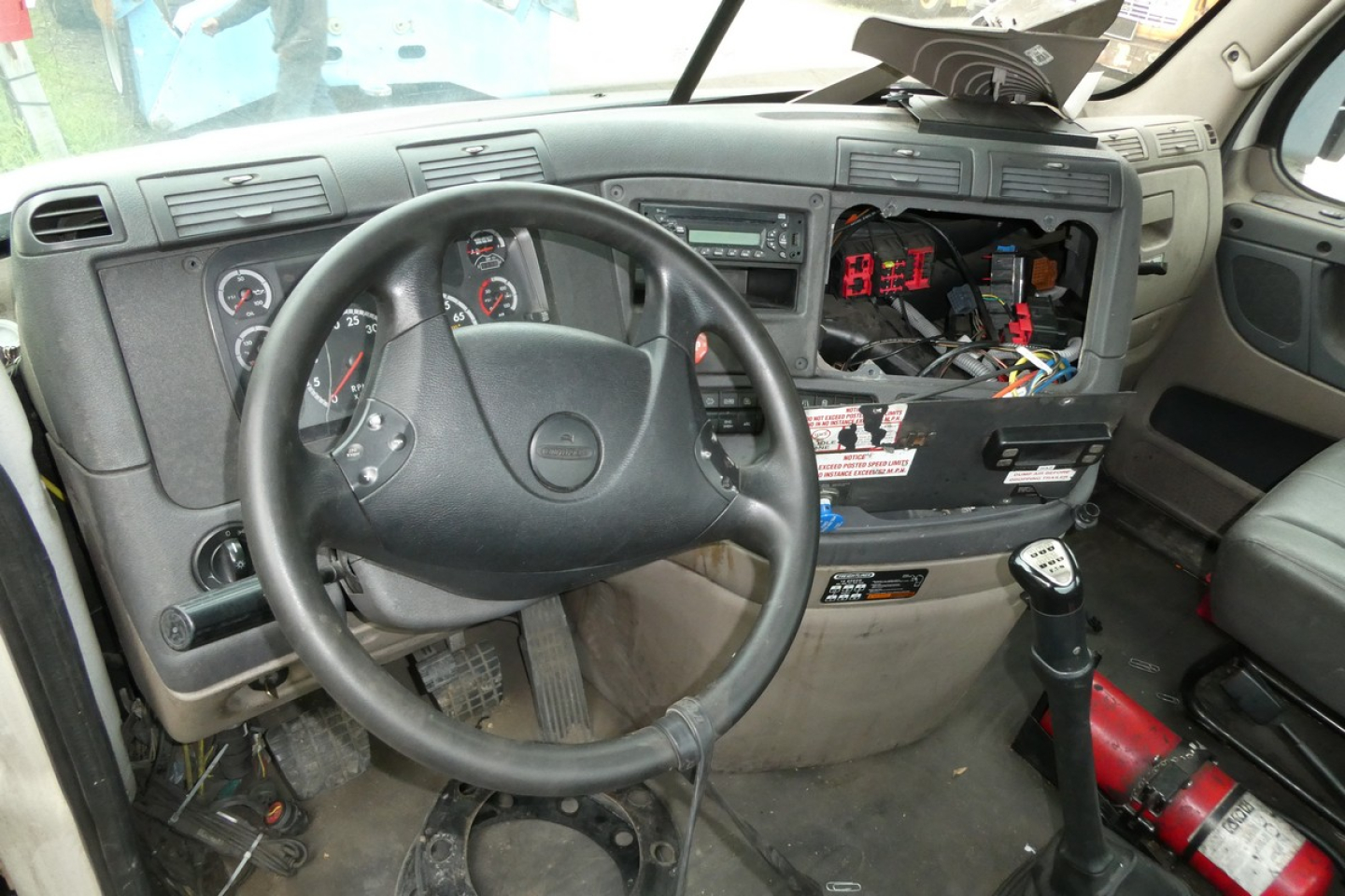 Dashboard area of a 2014 Freightliner Cascadia 113 cab with steering wheel, exposed instrument cluster, and exposed wiring under dash.