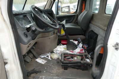 Truck cab interior showing steering wheel and dashboard with messy floor and removed seat components.