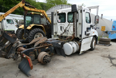 Truck cab and chassis of a Freightliner Cascadia 113 with exposed drivetrain and removed rear axle components in a yard.