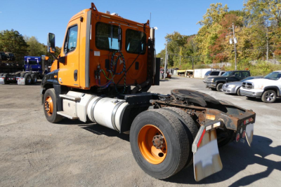Freightliner Cascadia 125 daycab tractor rear with orange cab, chassis, fuel tank, and mud flaps; VIN 1FUBGEDVXCLBK4301 on lot.