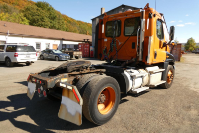 Orange Freightliner Cascadia 125 daycab truck rear view showing chassis, wheels, and cab; no engines visible.
