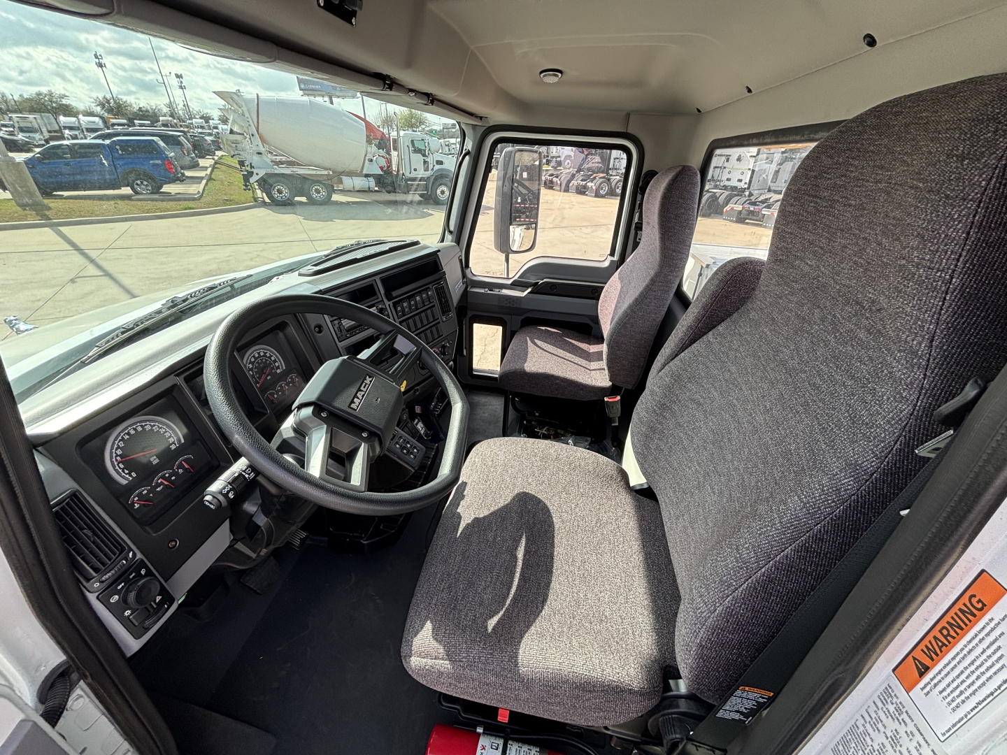 Interior of a new 2025 Mack MD7 truck cab showing steering wheel, dashboard, driver seat, and passenger seat in view.