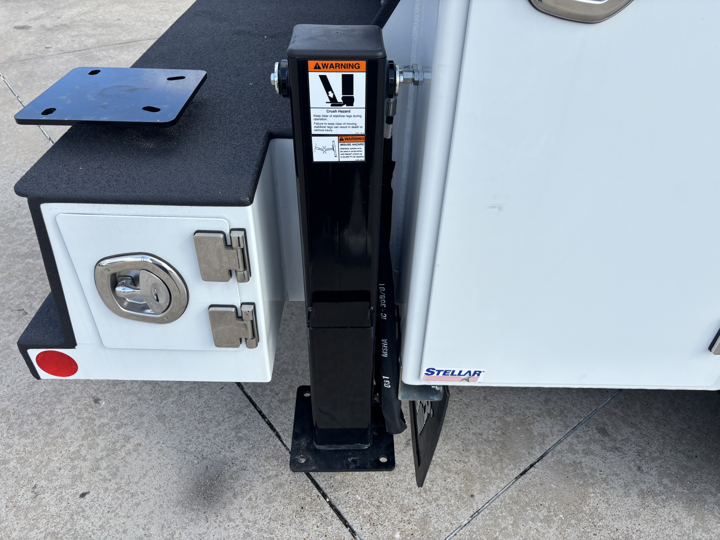 New 2025 Mack MD7 truck component detail showing mounting bracket and toolbox area with warning label on a vertical support.