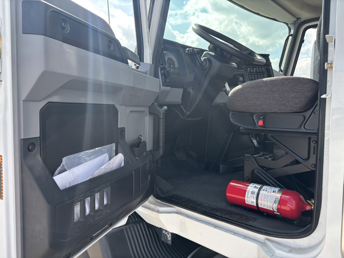 MD7 truck cabin interior showing driver seat, dashboard, steering wheel, and a red fire extinguisher on the floor near the door