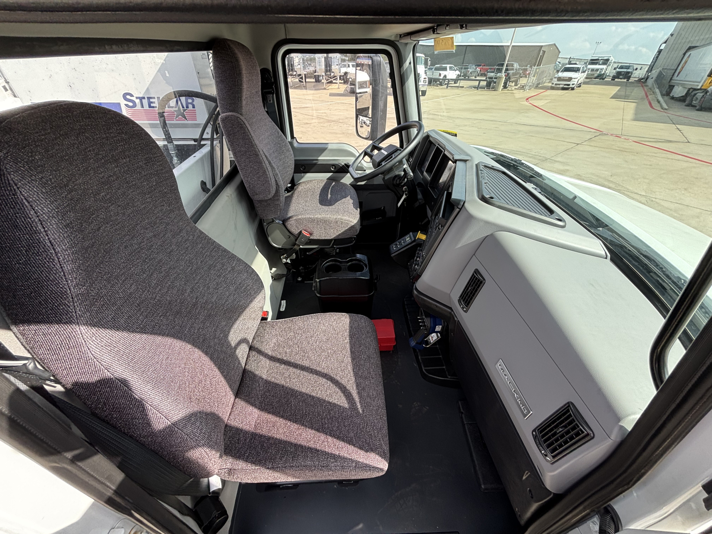 Driver cockpit of a 2025 Mack MD7 service/utility truck showing the steering wheel, dashboard with vents, and two front seats.