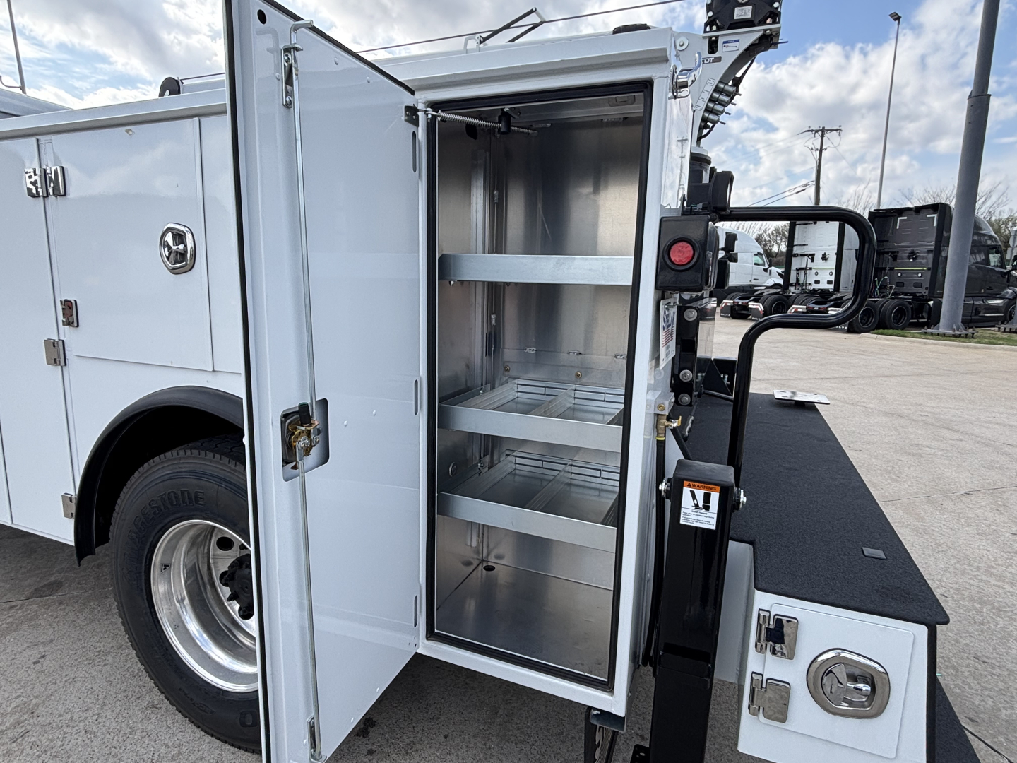 Truck service body cargo cabinet with open door showing multiple metal shelves in a Mack MD7 utility truck bed.