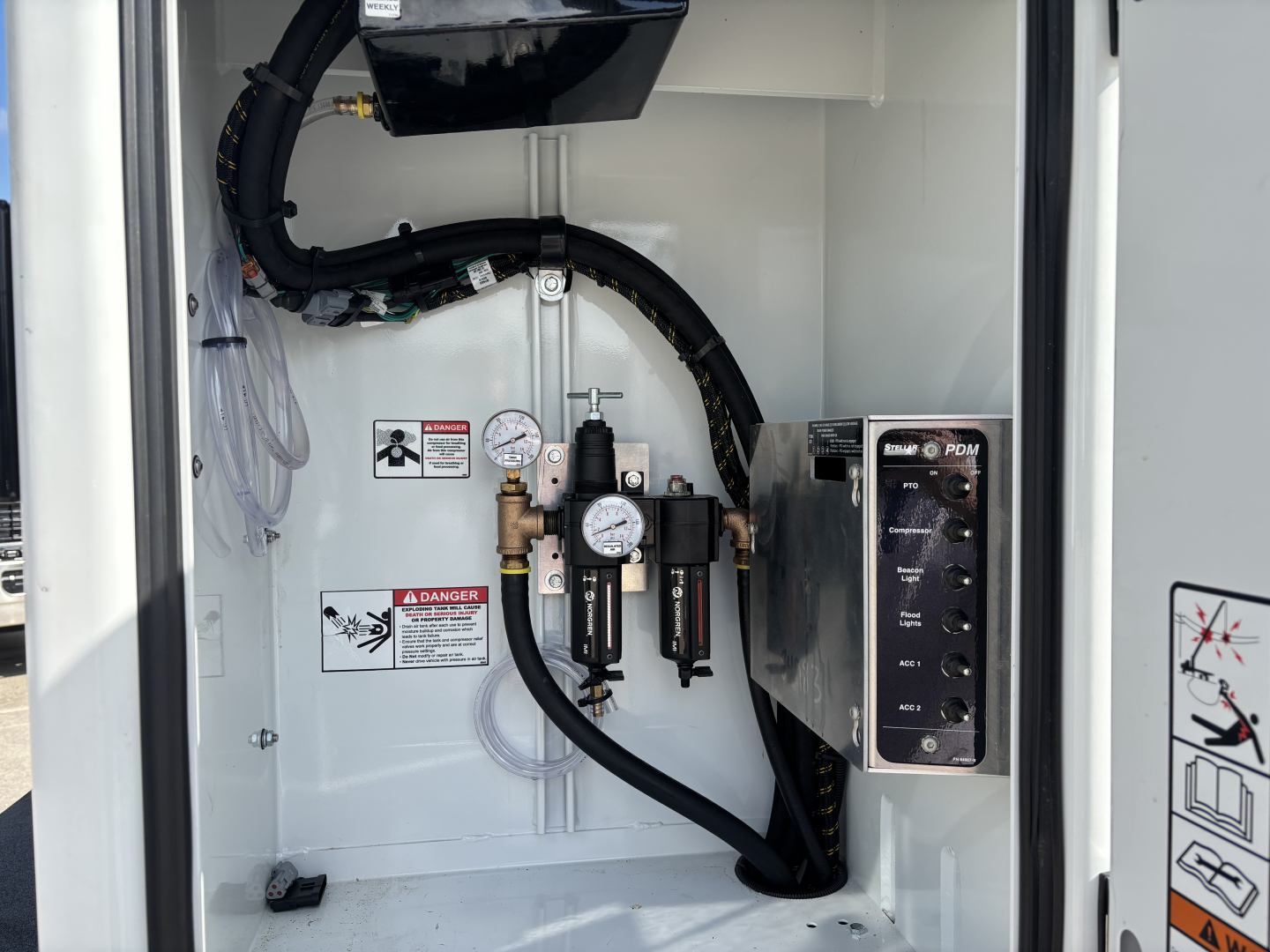 Panel inside a Mack MD7 service/utility truck showing gauges, hoses, and control switches. Visible text includes warning labels and a vertical panel with buttons