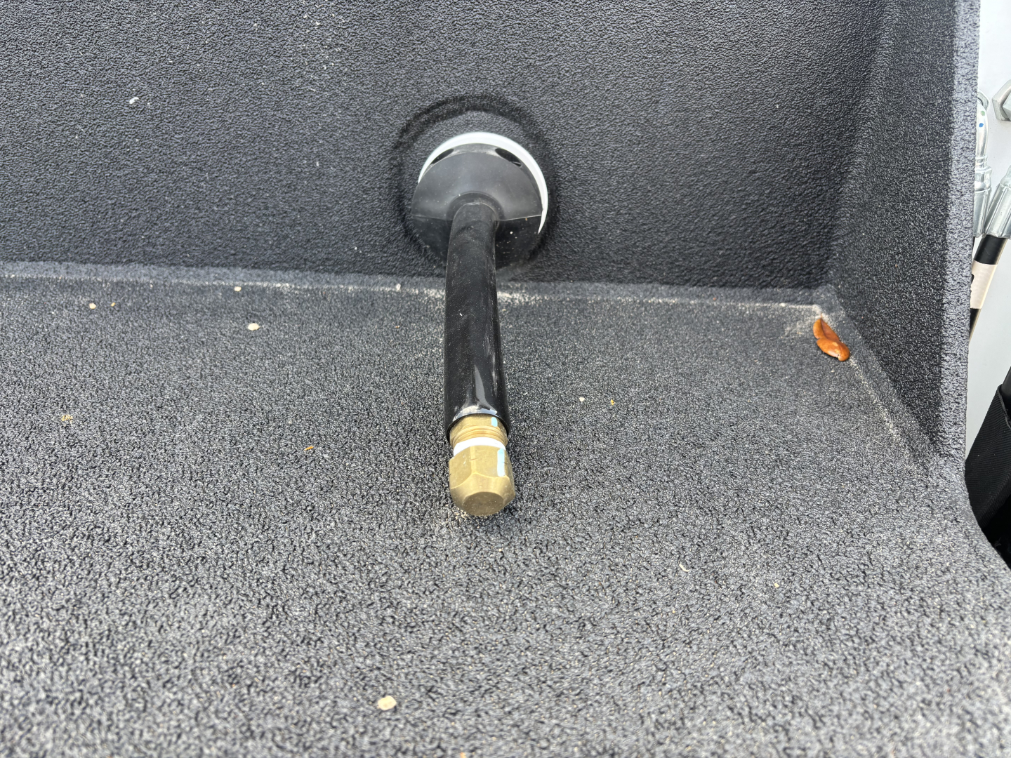 View of a Mack MD7 service body showing a brass hex air fitting or port at the rear with black hose or line attached, surrounding textured grey surface.