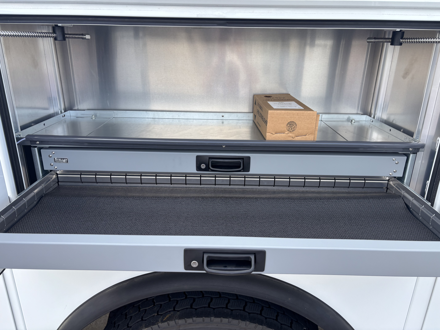 Mack MD7 service truck bed with open drawer showing empty storage compartment and small brown box inside.