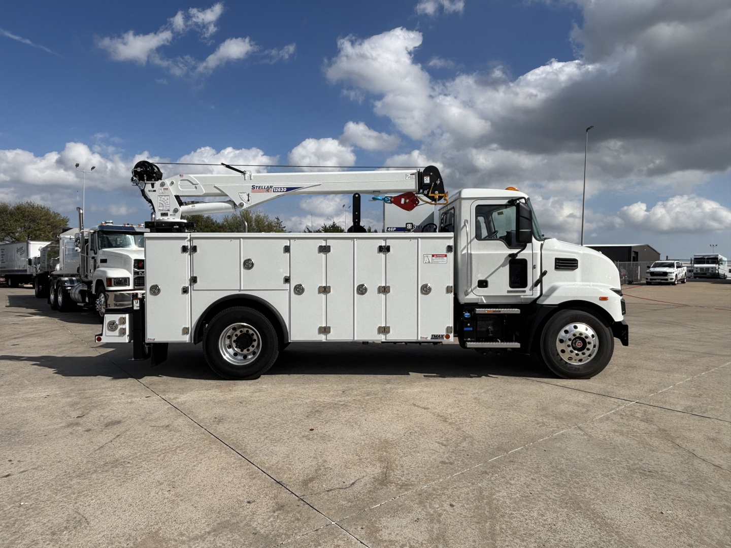 Mack MD7 service truck side view showing utility compartments and crane/boom on a clear day.