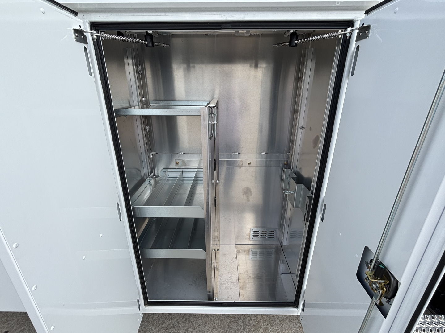 Empty stainless steel utility cabinet inside a truck bay with shelves and vented panels.
