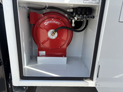 Service body rear showing a red Firestone/Firefighter-style air reel inside a white compartment with hoses; compact area with shelves and control panel visible.