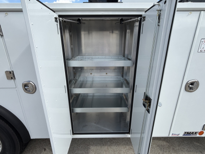Service body with open storage compartment showing four steel shelves inside a metal cabinet on a new Mack MD7 truck.