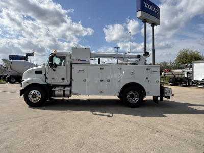 Service/utility truck in front of a Volvo dealership showing a white 2025 Mack MD7 service body with compartments and ladder rack.