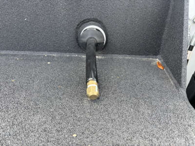 View of a Mack MD7 service body showing a brass hex air fitting or port at the rear with black hose or line attached, surrounding textured grey surface.