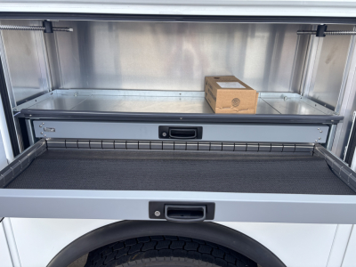 Mack MD7 service truck bed with open drawer showing empty storage compartment and small brown box inside.