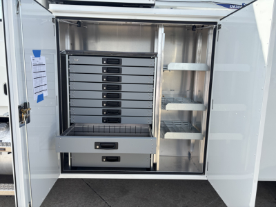 Truck utility body rear storage compartment with multiple drawers and shelves in an open cabinet.