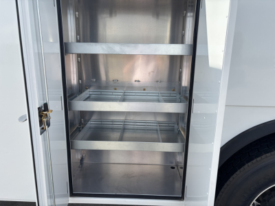 Storage compartment of a 2025 Mack MD7 service truck showing empty metal shelves inside a locker with a hinged door.