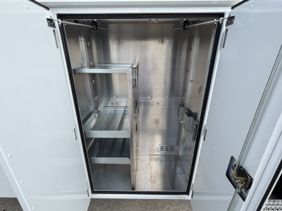 Empty stainless steel utility cabinet inside a truck bay with shelves and vented panels.