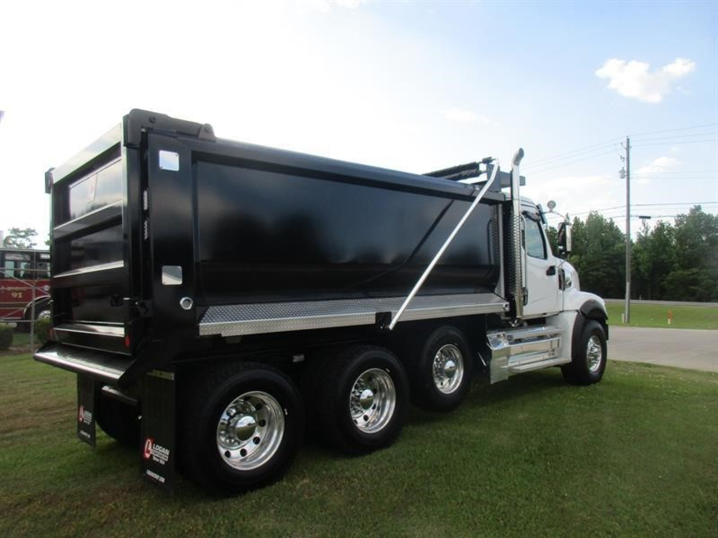 Dump truck showing three rear axles and a black dump bed with chrome wheels and white cab.