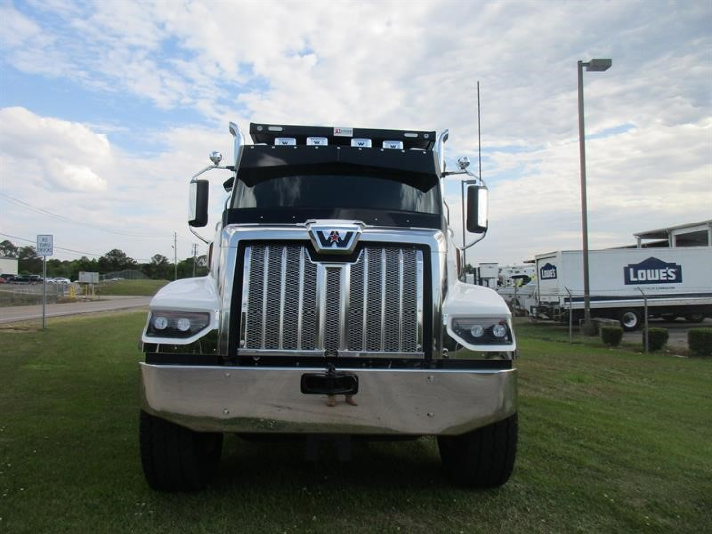 Front view of a 2026 Western Star 49X dump truck with chrome grille, large bumper, and elevated cab in a dealership lot.
