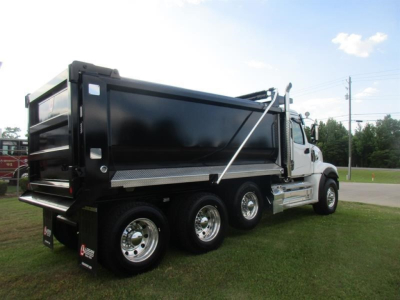 Dump truck showing three rear axles and a black dump bed with chrome wheels and white cab.