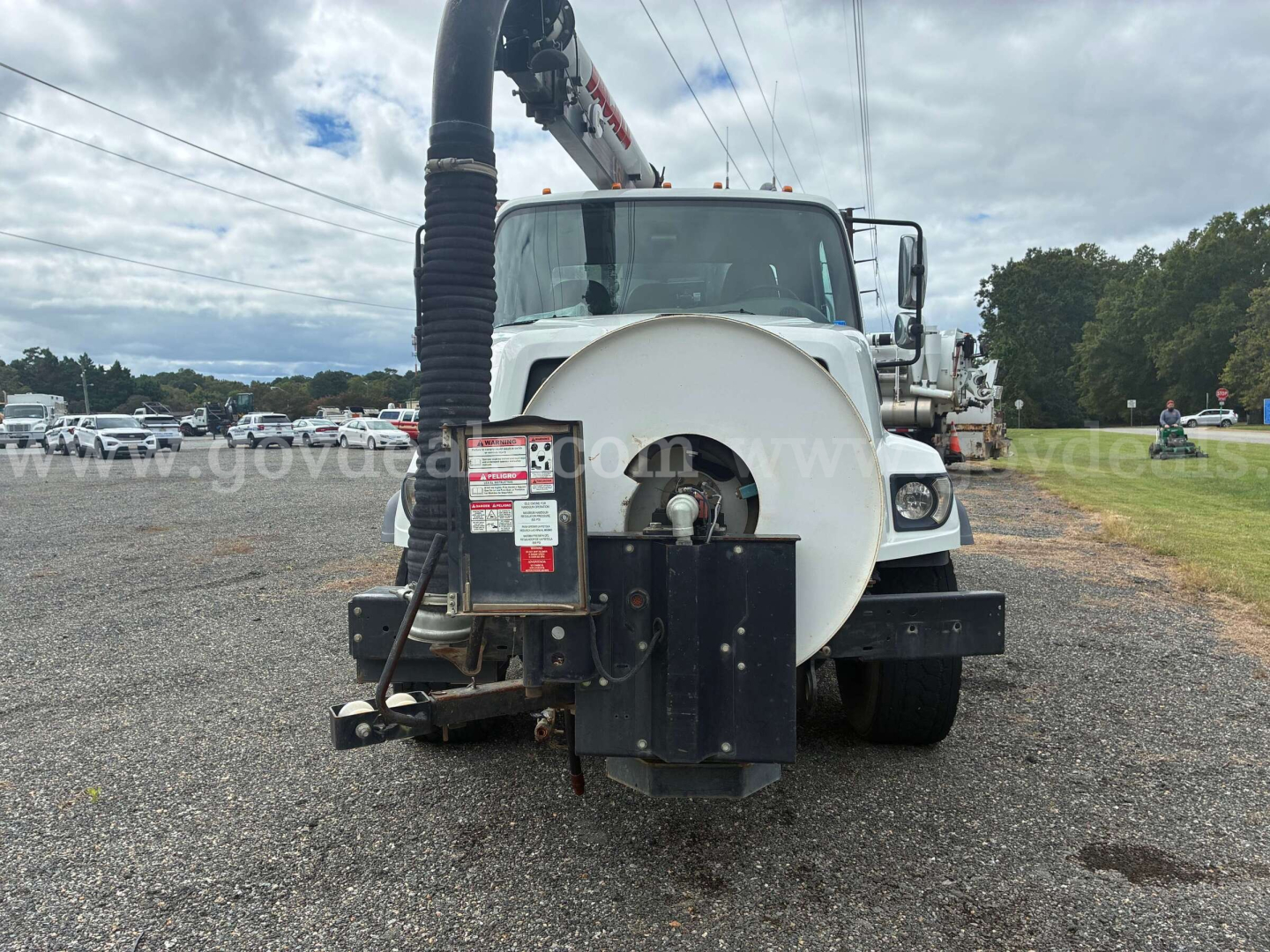 Front view of a white 2015 Freightliner 108SD vacuum truck with a large vacuum hose and rear-mounted equipment in a gravel lot.