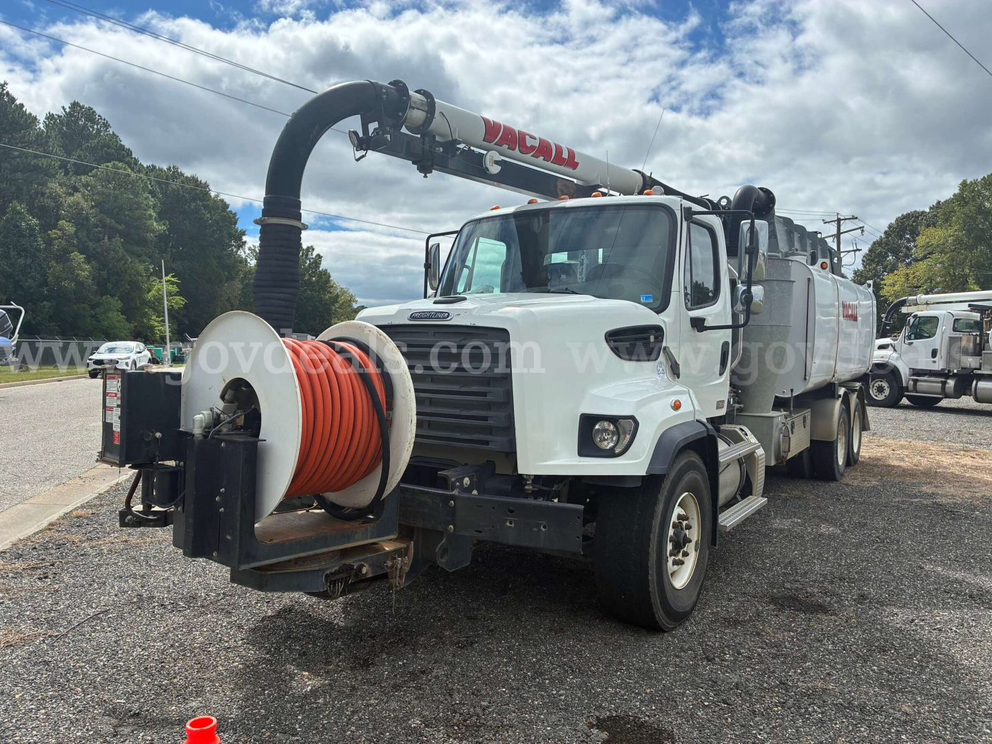 Truck-mounted vacuum trailer with large coiled hose reel andVacall vacuum arm, front grille, and cleaning unit visible.