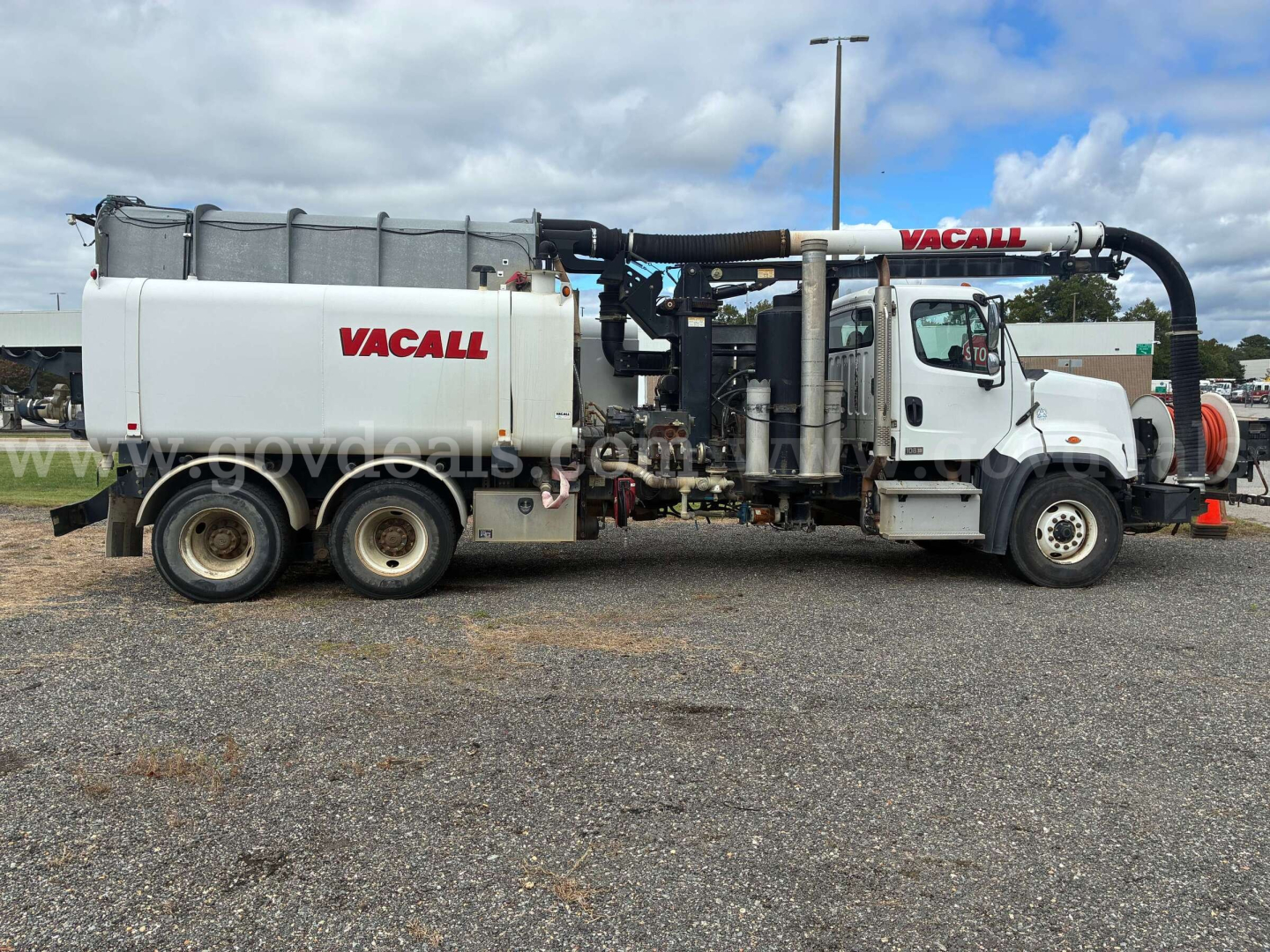 Vacall vacuum truck with white cab and tank, side view showing Vacall branding on hose reel and tank, engine bay and hydraulic components visible.