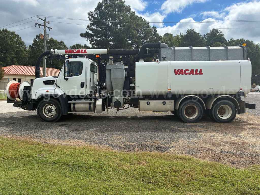 VacAll vacuum truck side view showing large white tank with VacAll logo and attached hoses, chassis, and cab in daylight.